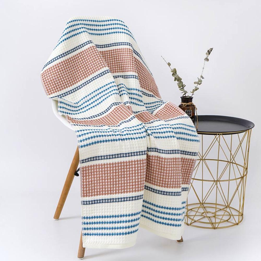 Cotton bath towel with white, blue, and rust-colored stripes in a honeycomb weave, draped over a chair.