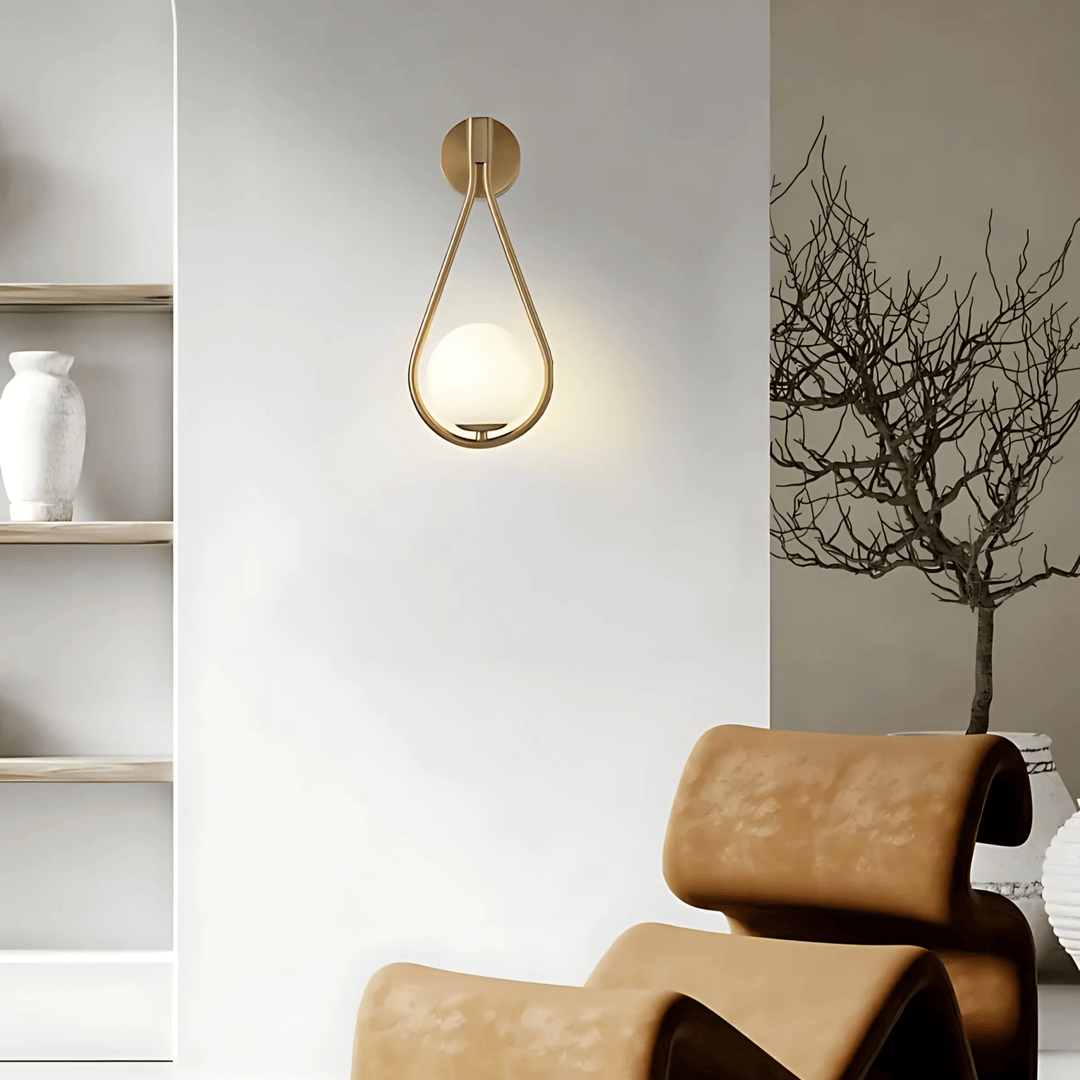 Gold teardrop wall sconce with a frosted glass globe, mounted on a white wall.