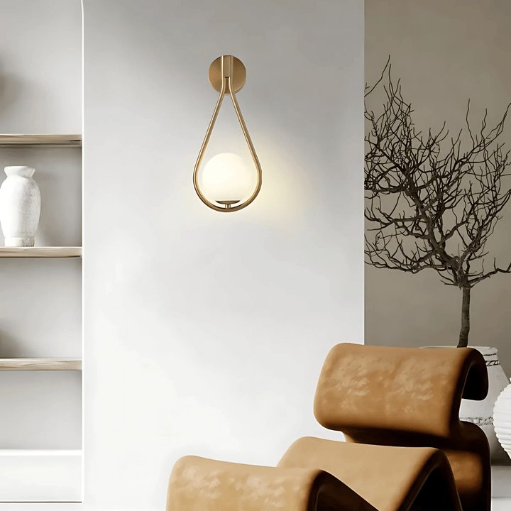 Gold teardrop wall sconce with a frosted glass globe, mounted on a white wall.