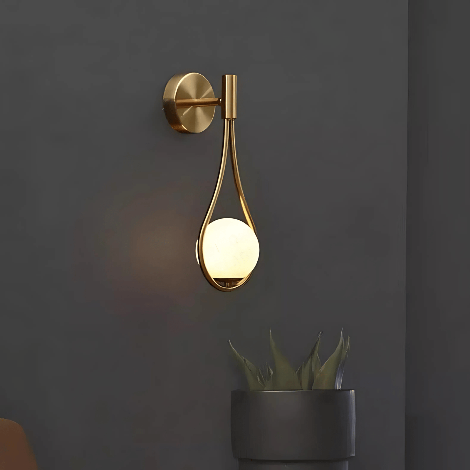 Gold teardrop wall sconce with a frosted globe light against a dark gray wall.