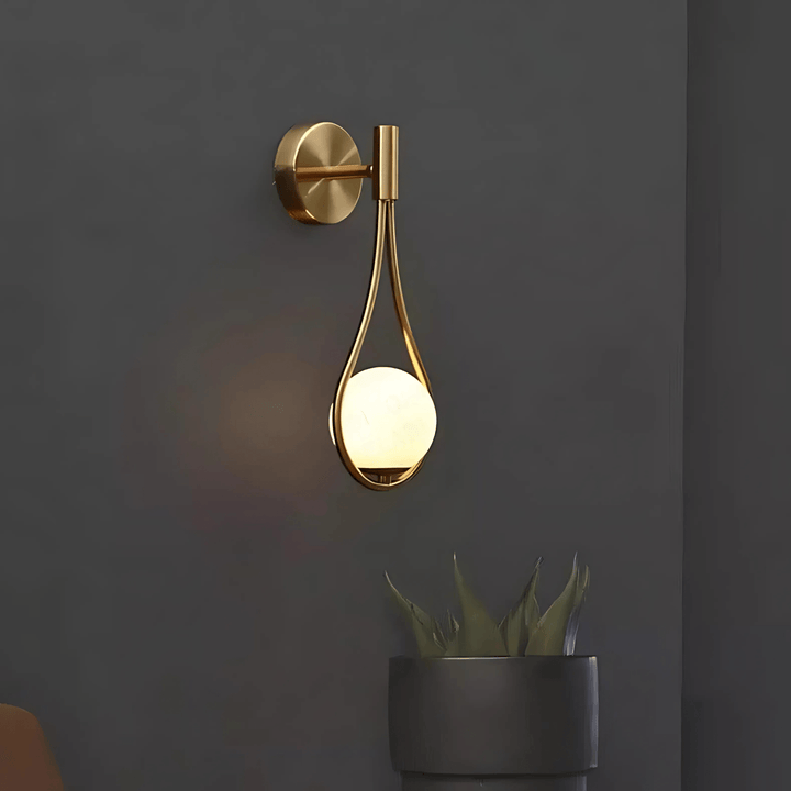 Gold teardrop wall sconce with a frosted globe light against a dark gray wall.