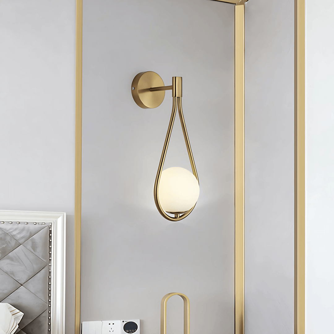 Gold teardrop wall sconce with a frosted white globe light against a light gray wall.
