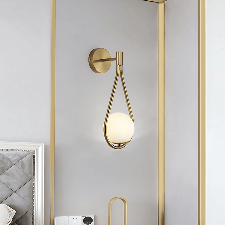 Gold teardrop wall sconce with a frosted white globe light against a light gray wall.