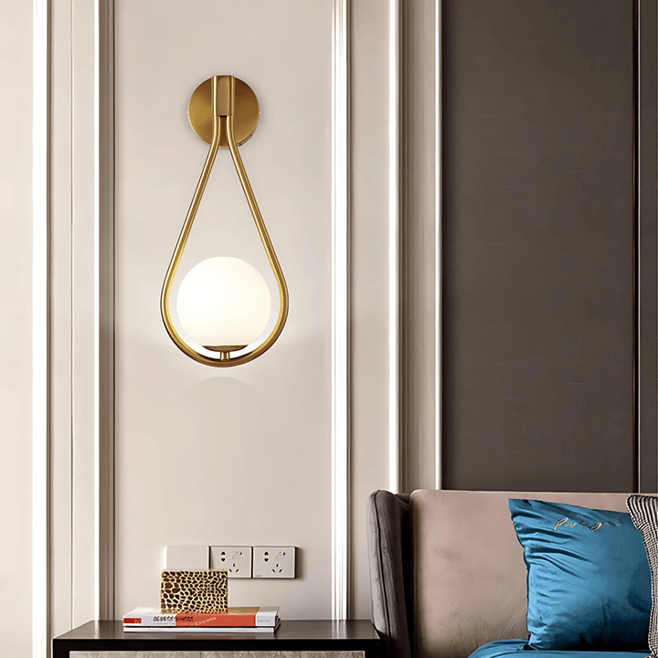 Teardrop wall sconce in gold with a frosted glass globe, mounted on a wall with decorative paneling.