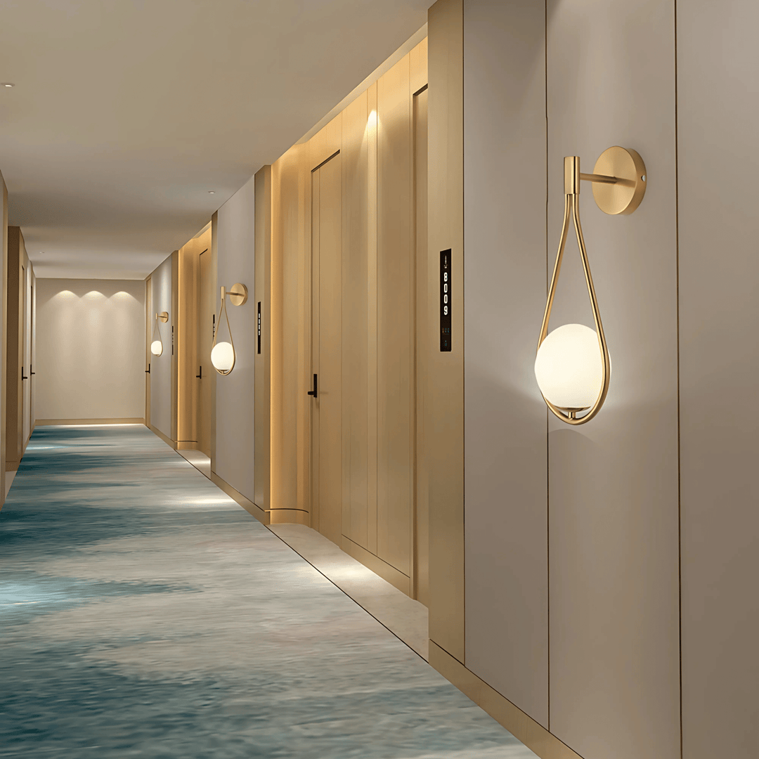 Teardrop wall sconce with a gold frame and a white globe light in a modern hallway.
