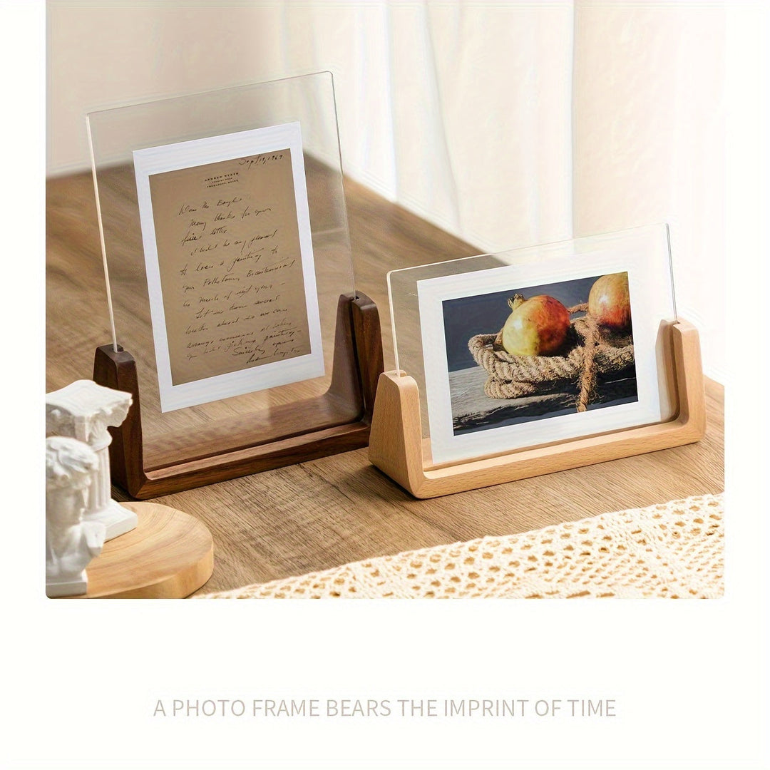 Two U-shaped acrylic photo frames with wooden bases displaying a letter and a photo of pomegranates on a wooden table.