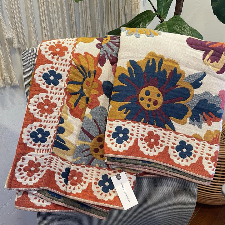 Reversible cotton bath towel with a bold floral print in blue, yellow, orange, and purple on a cream background.