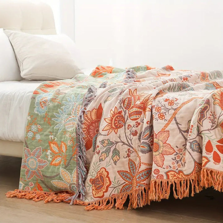 Rustic floral boho cotton blanket with tassels draped on a bed.