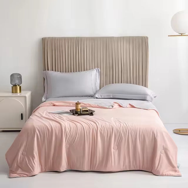 A pink Forevercool cooling blanket is draped over a bed with gray pillows and a pleated headboard.