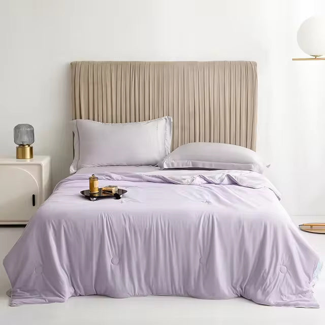 Lavender cooling blanket with two pillows and a bedside tray on a bed with a pleated headboard.