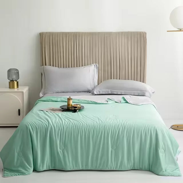 A mint green Forevercool cooling blanket is neatly spread on a bed with gray pillows.