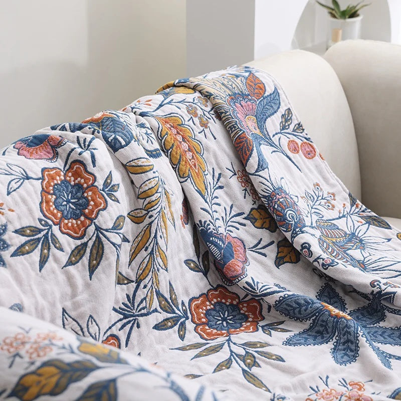 Rustic artistic flora cotton blanket draped over a sofa, featuring a detailed floral pattern in blue, orange, and yellow.