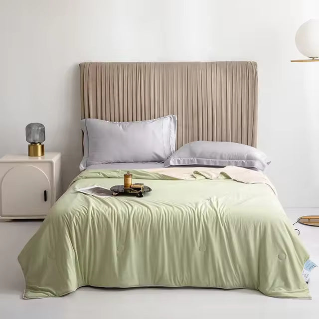 A light green Forevercool cooling blanket is draped over a bed with light gray pillows and a pleated headboard.