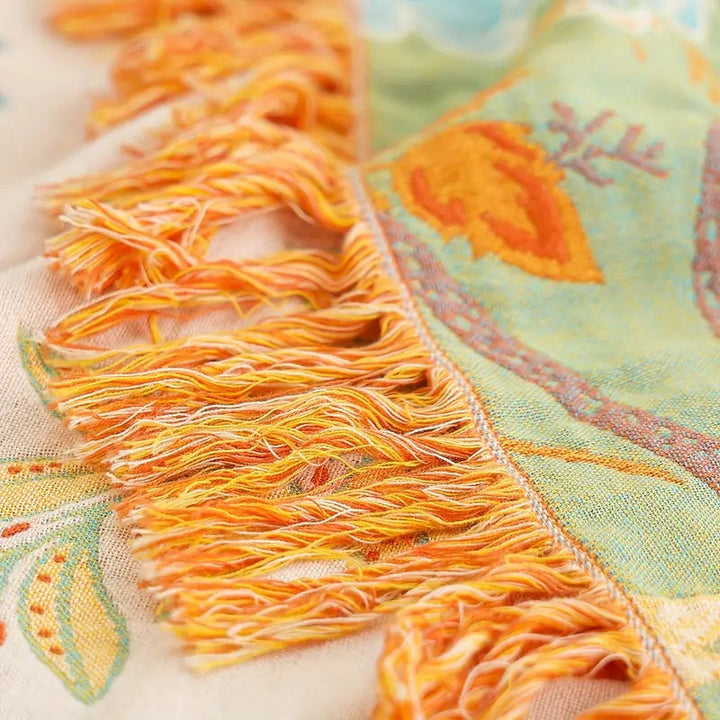 Close-up of a rustic floral boho cotton blanket with orange and yellow tassels.