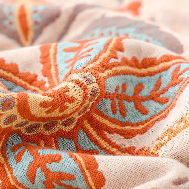 Close-up of a rustic floral boho cotton blanket with orange, blue, and cream paisley patterns.