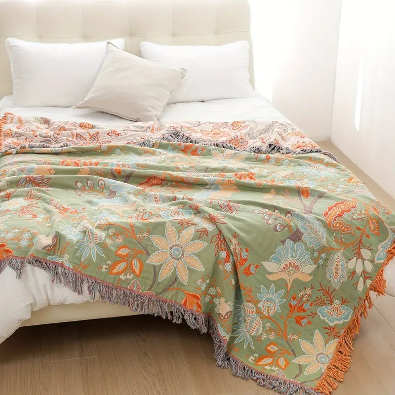 Green cotton blanket with a rustic floral pattern and fringed edges, draped on a bed.