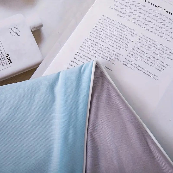 A light blue and grey cooling blanket draped over an open book.