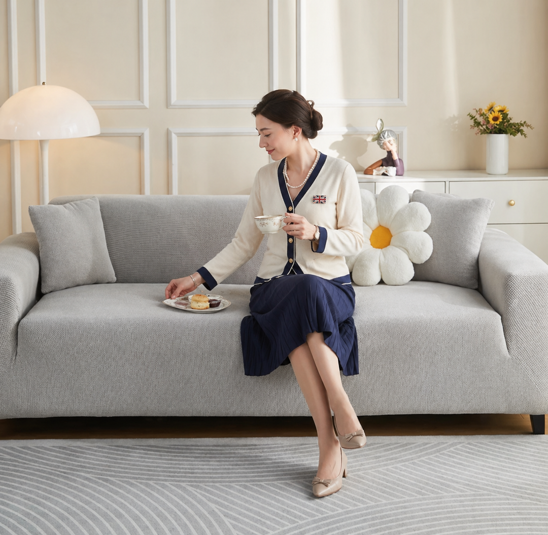 A woman sits on a light grey couch covered by a narrow jacquard couch cover, holding a teacup.