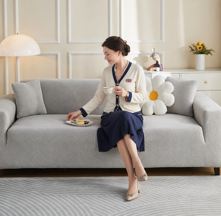 A woman sits on a light grey couch covered by a narrow jacquard couch cover, holding a teacup.