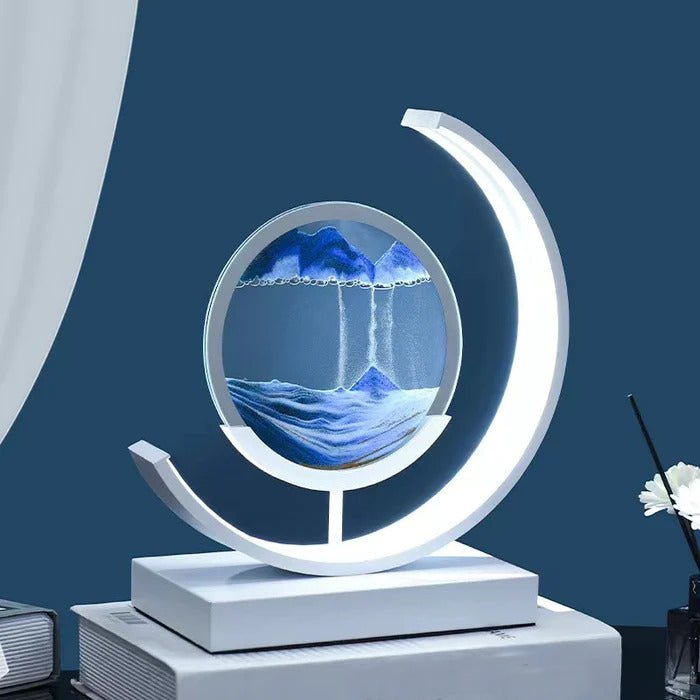 Quicksand LED table lamp with a crescent moon-shaped light illuminating a circular glass enclosure with falling sand.