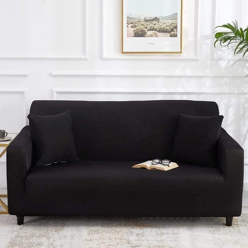 Black adaptable couch cover with two throw pillows and an open book with glasses on it.