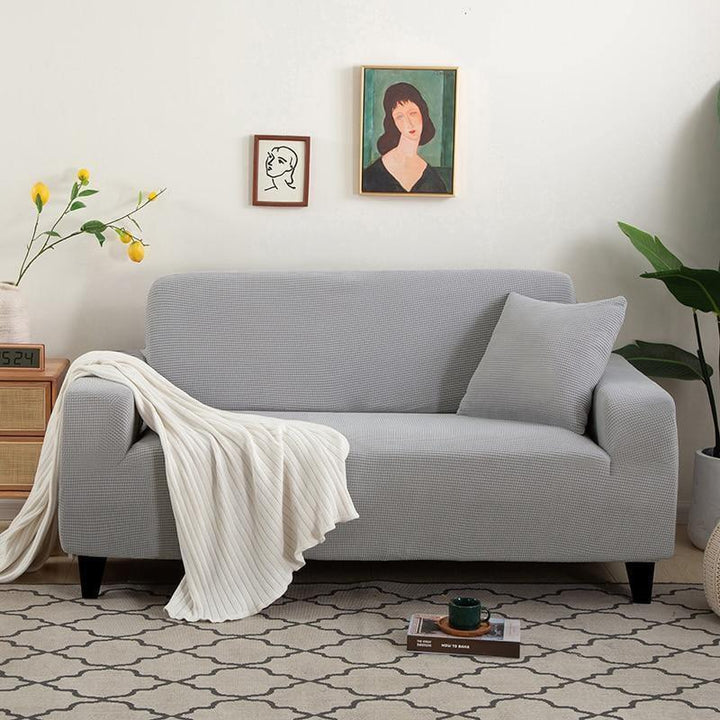 Light grey narrow jacquard couch cover with a textured pattern, a white throw blanket, and a grey pillow.