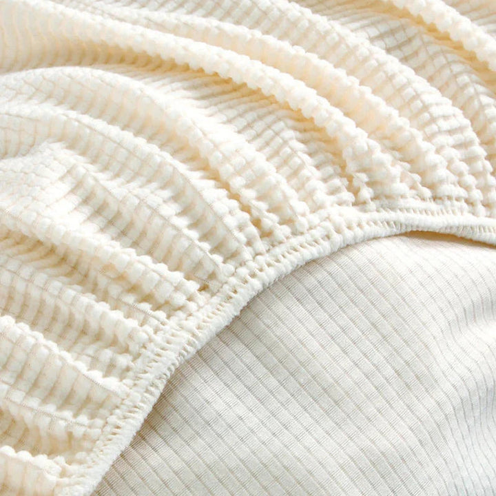 Close-up of a white jacquard couch cover with a textured pattern and elastic binding.