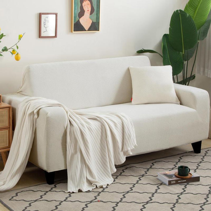 White narrow jacquard couch cover with a textured pattern, draped over a sofa with a throw blanket and pillow.