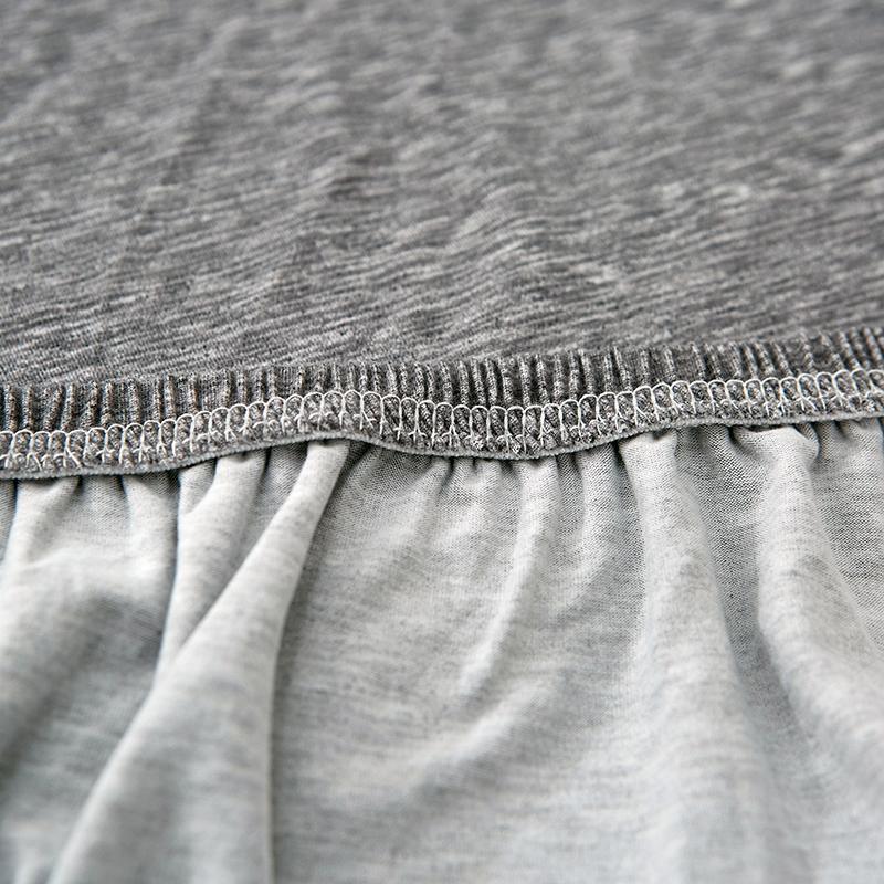 Close-up of a light grey spotted L-shaped sofa cover showing the elasticized hem and fabric texture.