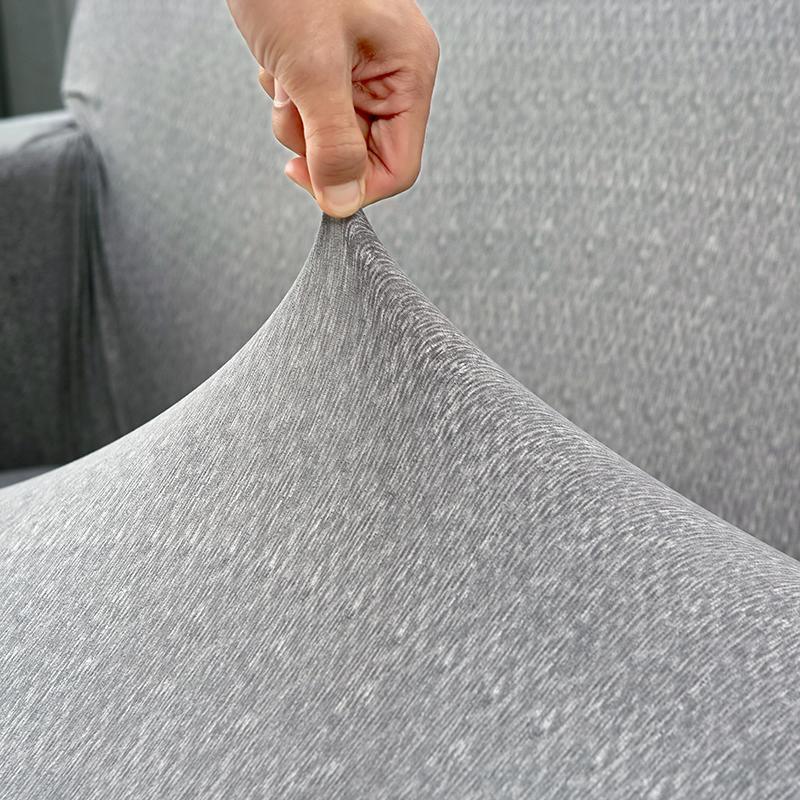 Hand stretching a light grey spotted L-shaped sofa cover to show its adaptable fit.