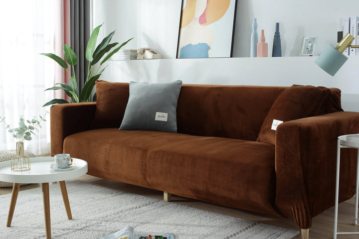 Brown velvet couch cover draped over a sofa, with a grey pillow and a small white table in front.