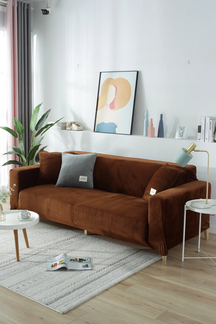 Brown velvet couch cover on a sofa with a grey pillow and a small white side table.
