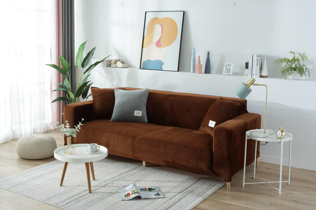 Brown velvet couch cover on a sofa with decorative pillows and a side table.