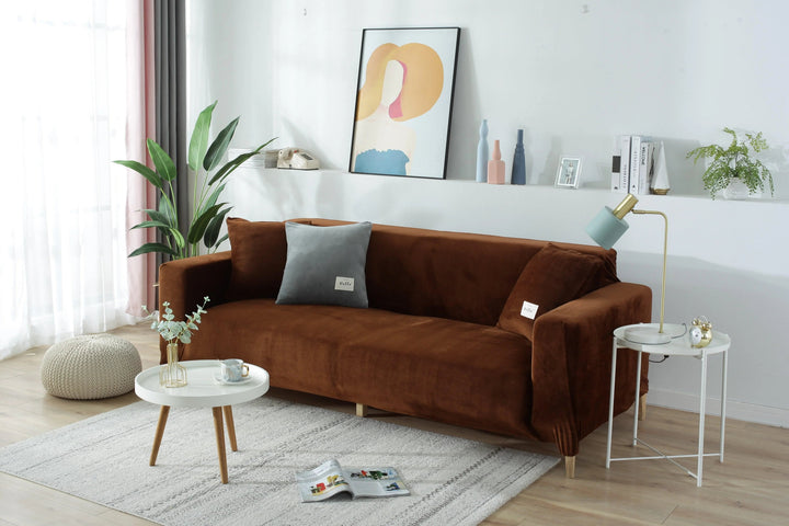 Brown velvet couch cover on a sofa with decorative pillows and a side table.