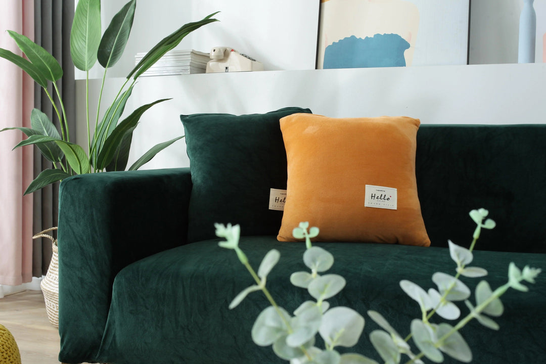 Dark green velvet couch cover draped over a sofa with orange and green pillows.
