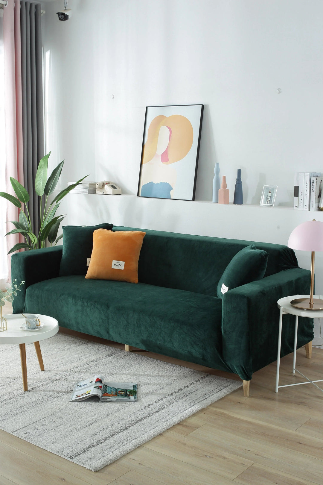 Dark green velvet couch cover on a sofa with an orange pillow and a small white table with a cup.