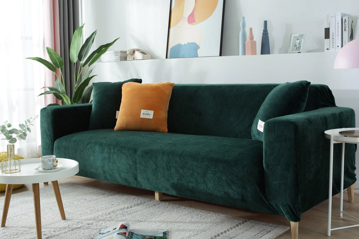 A dark green velvet couch cover fitted on a sofa with an orange accent pillow.