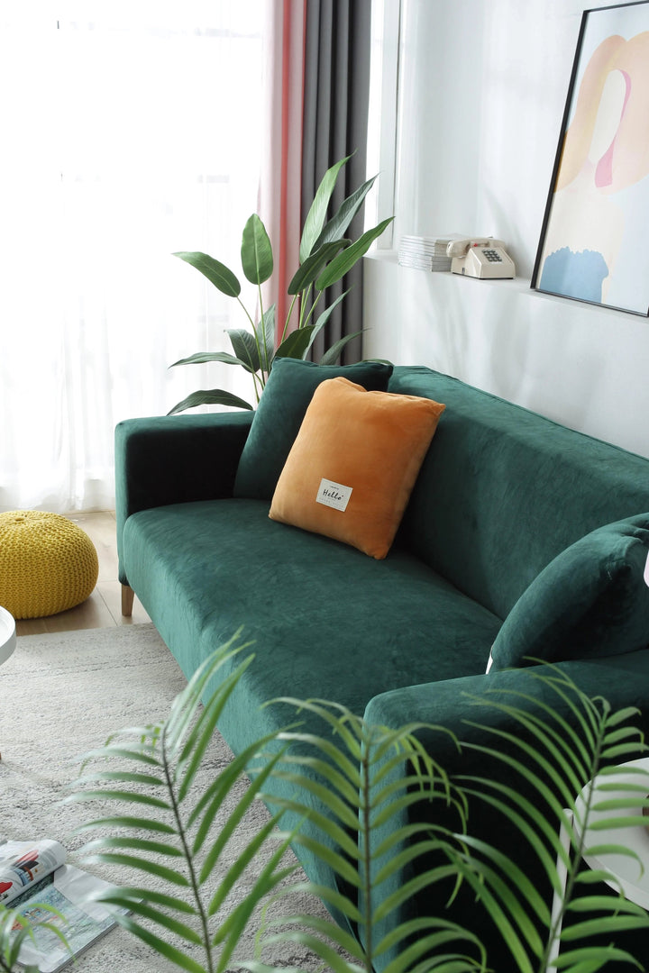 Dark green velvet couch cover with an orange accent pillow and a yellow ottoman.
