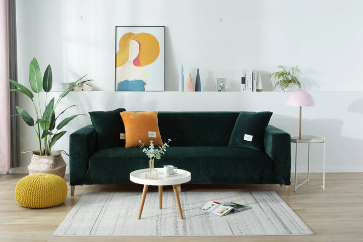 Dark green velvet couch cover on a sofa with decorative pillows and a small table.