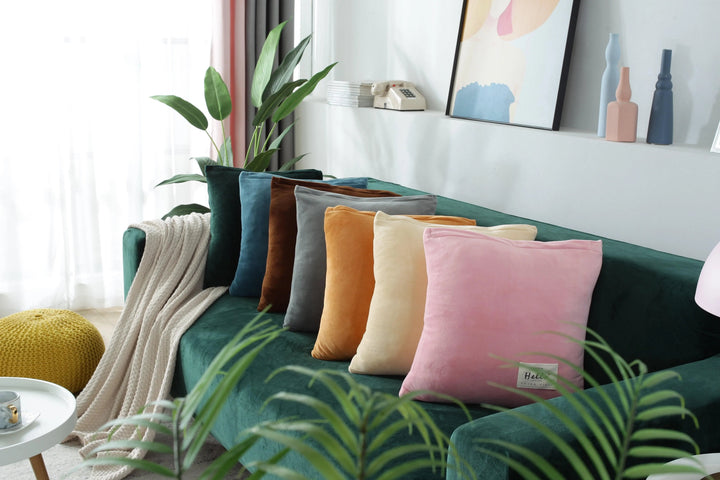 A dark green velvet couch with an assortment of colorful throw pillows and a cream-colored throw blanket.