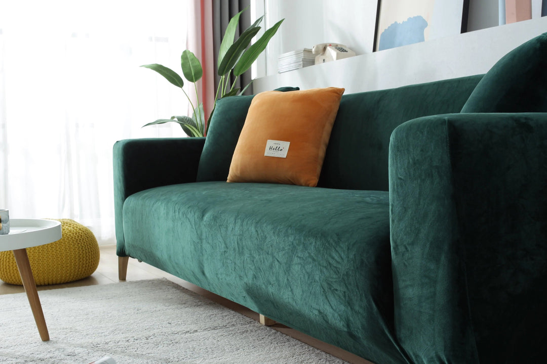 Dark green velvet couch cover draped over a sofa with an orange accent pillow.