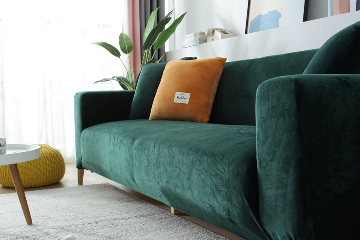 Dark green velvet couch cover draped over a sofa with an orange accent pillow.