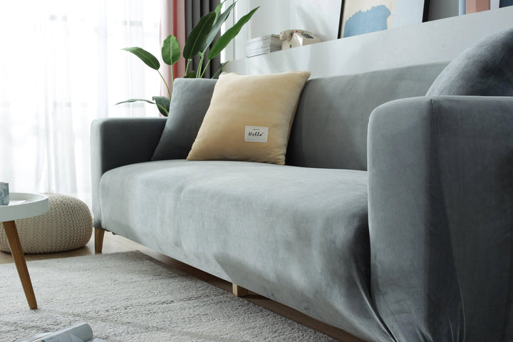 Light grey velvet couch cover draped over a sofa with two decorative pillows.