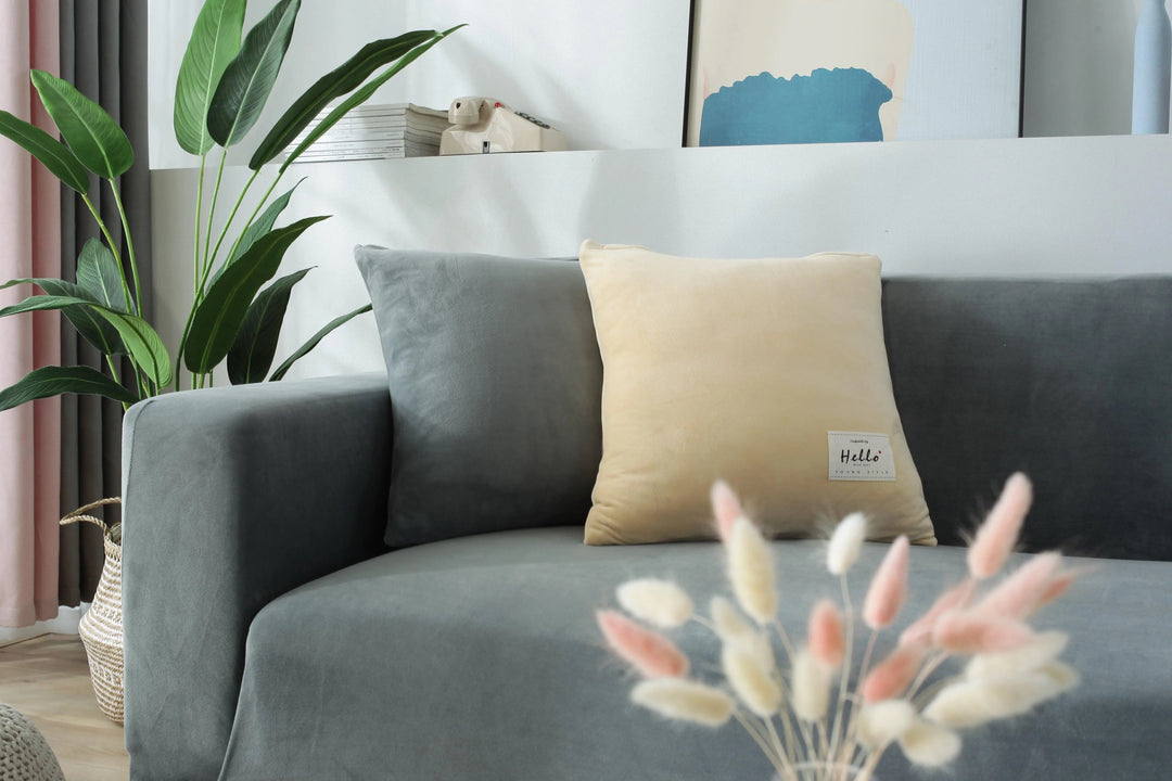 A light grey velvet couch cover is draped over a sofa, with a cream-colored pillow on top.