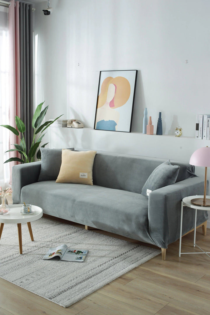 Light grey velvet couch cover on a sofa with accent pillows and a small side table.