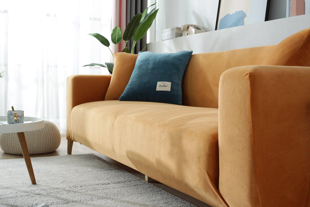 Orange velvet couch cover with a blue accent pillow on a sofa.