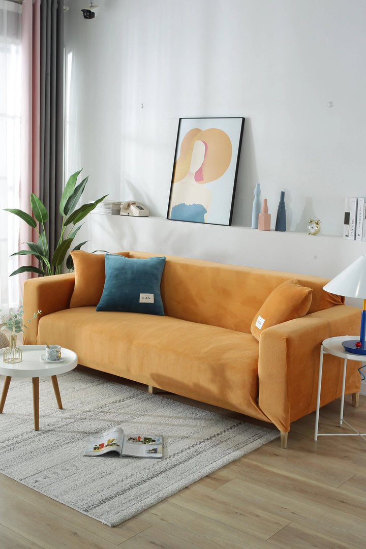 Orange velvet couch cover on a sofa with blue and orange pillows.