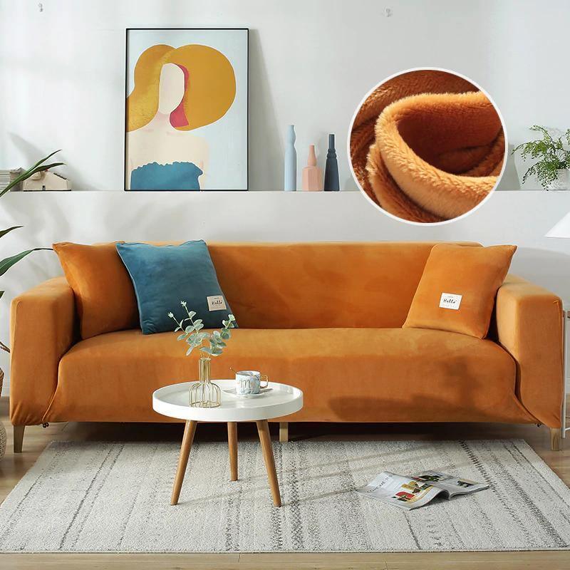 Orange velvet couch cover draped over a sofa with blue accent pillows and a white coffee table.