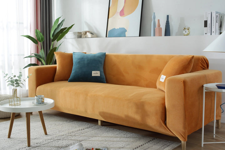 A vibrant orange velvet sofa cover fitted on a three-seater couch in a bright living room.