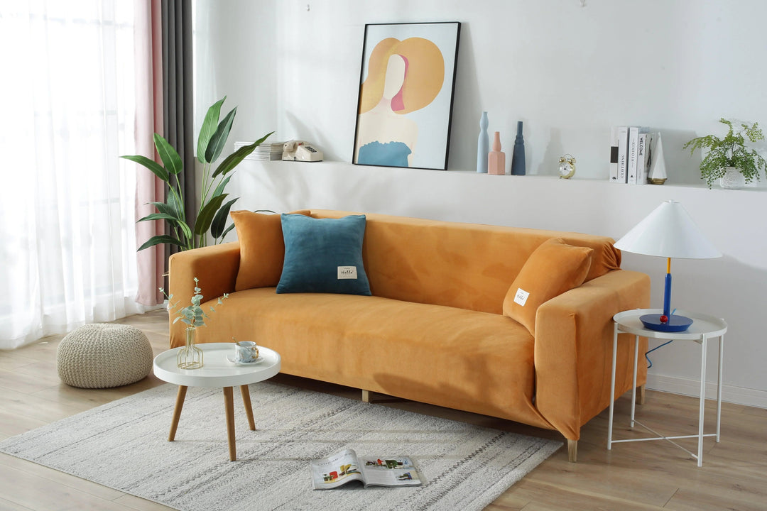Orange velvet sofa cover draped over a sofa, with decorative pillows and a side table.